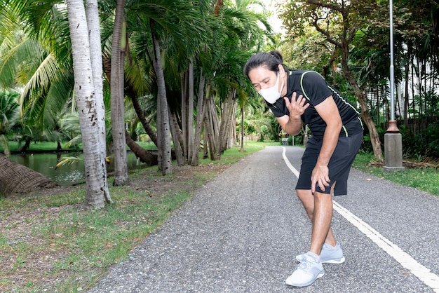 Azjatycki mężczyzna ma ucisk w klatce piersiowej duszność od noszenia maski podczas biegania w parku