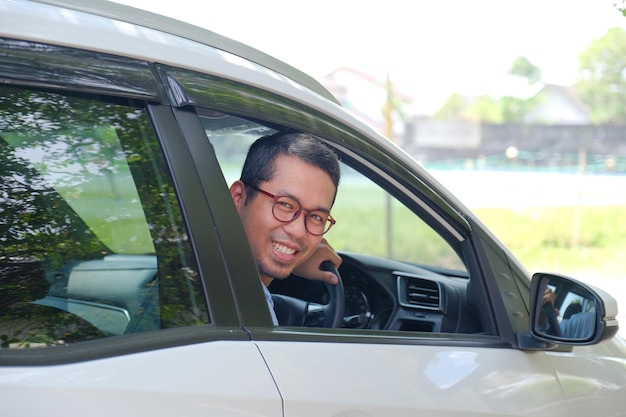 Azjatycki mężczyzna patrzący za siebie z wnętrza swojego samochodu z radosnym wyrazem twarzy