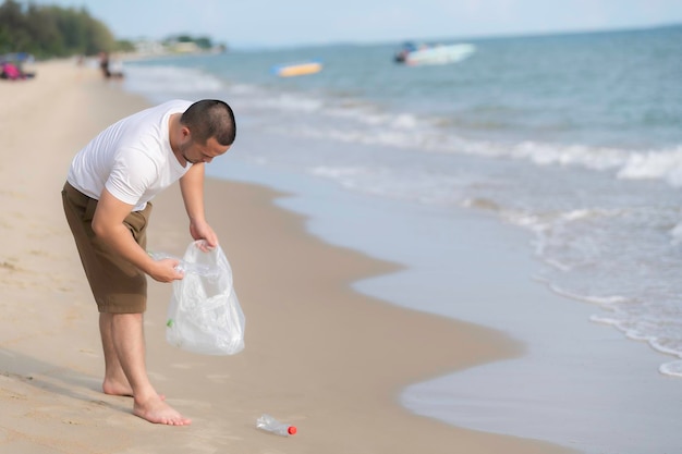 Azjatycki mężczyzna przechowuje śmieci na wewnętrznej plaży morskiej. Wolontariusze trzymają plastikowe butelki śmieci