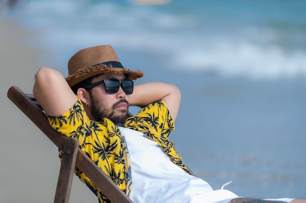 Azjatycki mężczyzna siedzący na krześle na plaży wewnątrz morzaCzas relaksu w lecie
