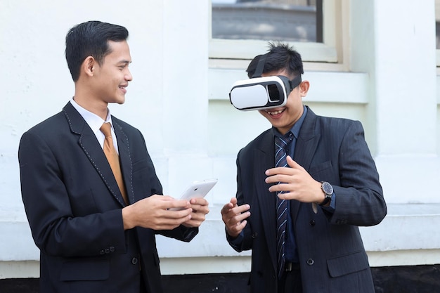 Azjatycki mężczyzna w garniturze noszący i ustawiający okulary VR i smartfon typu tablet, technologia urządzeń cyfrowych
