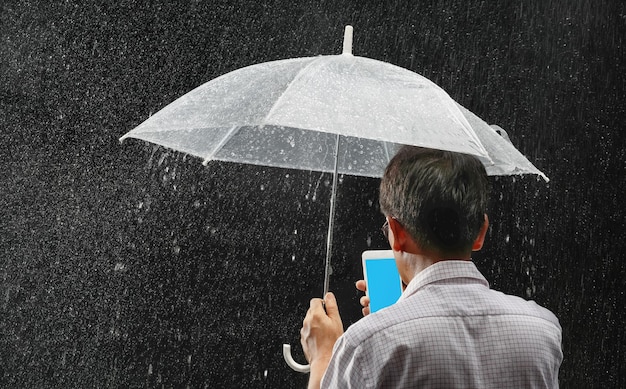 Azjatycki mężczyzna w średnim wieku trzymający parasol i telefon w deszczu w nocy