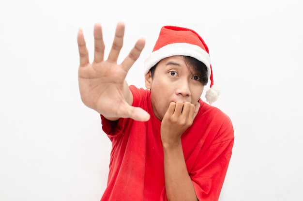 Azjatycki mężczyzna w świątecznych ubraniach santa hat jest przerażony zasłaniając usta i drżąc.