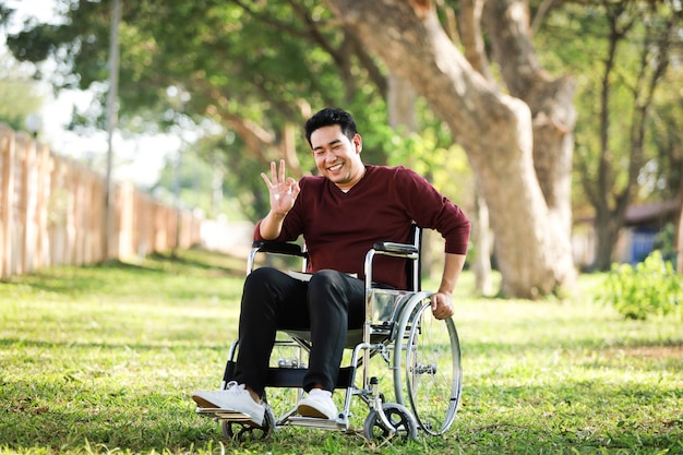 Azjatycki młodego człowieka obsiadanie na wózku inwalidzkim w parkowym szpitalu