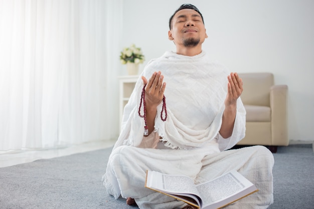 Azjatycki młody człowiek modli się z Al-Koranem i koralikami do modlitwy