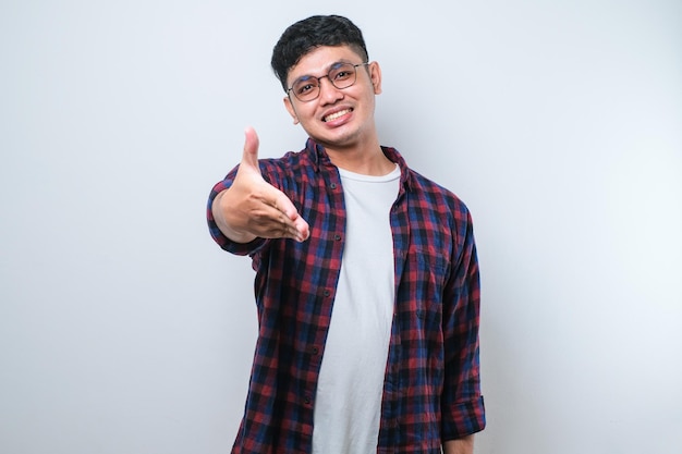 Azjatycki młody człowiek uśmiechający się przyjaźnie oferując uścisk dłoni jako powitanie i powitanie udanego biznesu