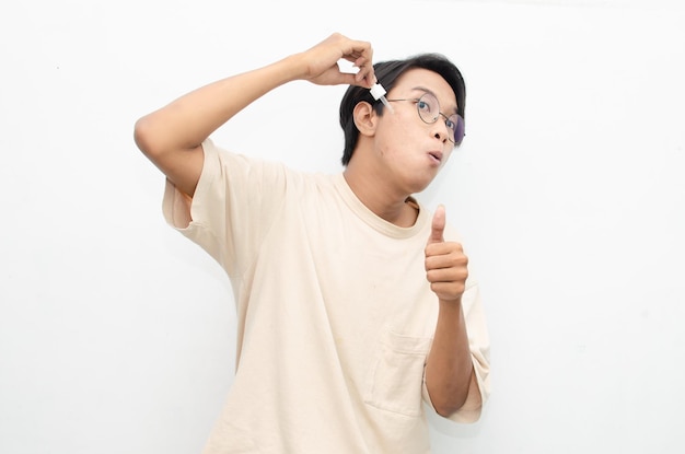 azjatycki młody człowiek w swobodnej beżowej koszulce nakładający serum kosmetyczne na trądzik za pomocą pipety