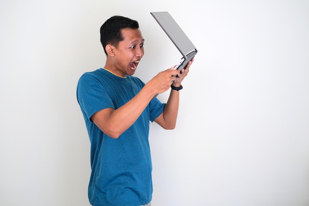 Azjatycki młody człowiek z gniewnym wyrazem twarzy i rzuca laptopem na białym tle