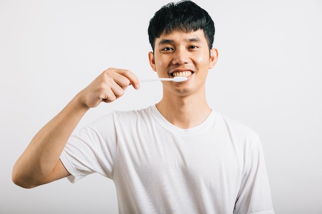 Azjatycki młody mężczyzna pewnie myje zęby rano, promując zdrowie zębów Portret szczęśliwego tajskiego nastolatka z szczoteczką do zębów w zdjęciu studyjnym izolowanym na białym tle