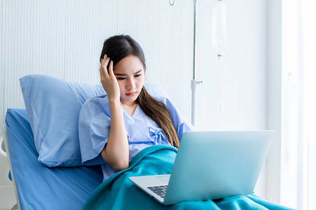 Azjatycki młody żeński pacjent ma headach na łóżku z laptopem na nim