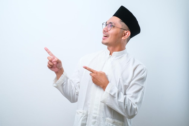 Azjatycki muzułmanin ma wskazujący coś na bok obiema rękami na białym tle