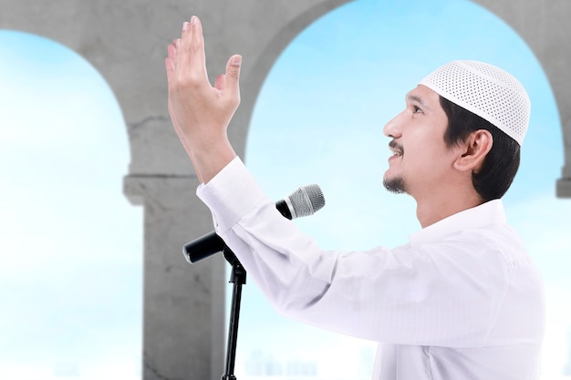 Azjatycki Muzułmanin Stojąc, Podnosząc Ręce I Wygłaszając Kazanie Na Temat Meczetu