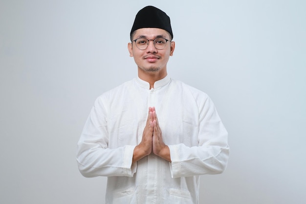 Azjatycki muzułmanin w okularach uśmiechający się, aby pozdrowić podczas obchodów Ramadanu i Eid Al Fitr na białym tle