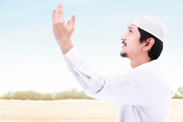 Azjatycki muzułmański mężczyzna stojący, podczas gdy podniósł ręce i modlił się na tle błękitnego nieba