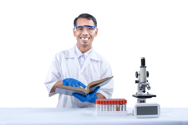 Azjatycki nerd naukowiec stojący i trzymający książkę z mikroskopem i stojakiem na probówki medyczne na biurku na białym tle nad białym tłem