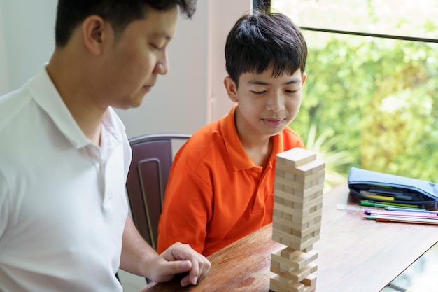 Zdjęcie azjatycki ojciec i syn grają w grę z klocków drewnianych beztroskie dziecko bawi się w grę z klocków drewnianych w konstruktora z klocków z ojcem w domu