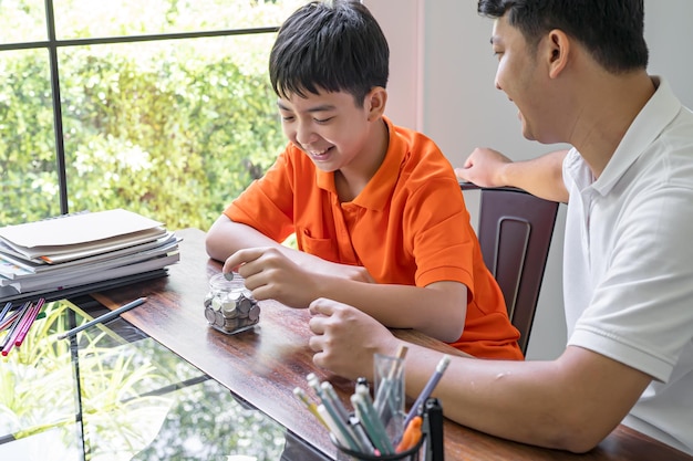 Azjatycki ojciec i syn uczą syna umiejętności finansowych, oszczędzając pieniądze Tata i dzieci wrzucają pieniądze do ojcostwa skarbonki