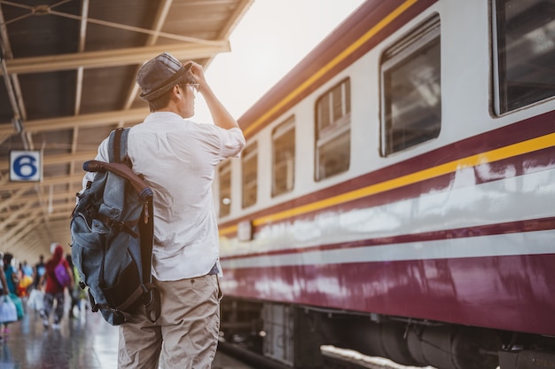 Azjatycki podróżnik z plecakiem czeka na pociąg, azjatycki backpacker w kapeluszu stojący na peronie kolejowym na stacji kolejowej w Bangkoku. Wakacje, podróż, podróż i lato Koncepcja podróży.