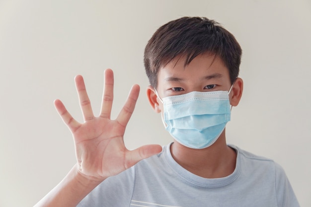Azjatycki preteen boy noszący medyczną maskę na twarz i robiąc znak stopu, samo-kwarantanna, koronawirus, epidemia epidemii wirusa covid-19