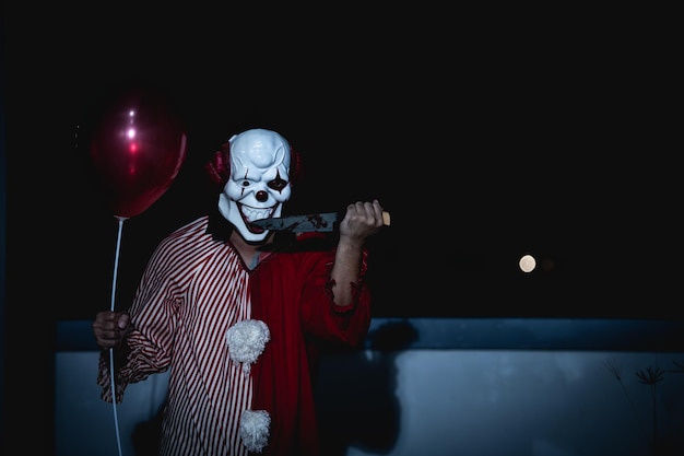 Azjatycki przystojny mężczyzna nosi maskę klauna z bronią na scenie nocnejKoncepcja festiwalu HalloweenHorror przerażające zdjęcie zabójcy w pomarańczowym ubraniuZły charakter klauna