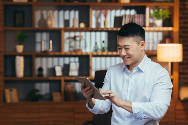 Azjatycki relaks w domu po pracy oglądając kanał wideo online na tablecie uśmiechnięty i radujący się człowiek biznesu czytający ebook