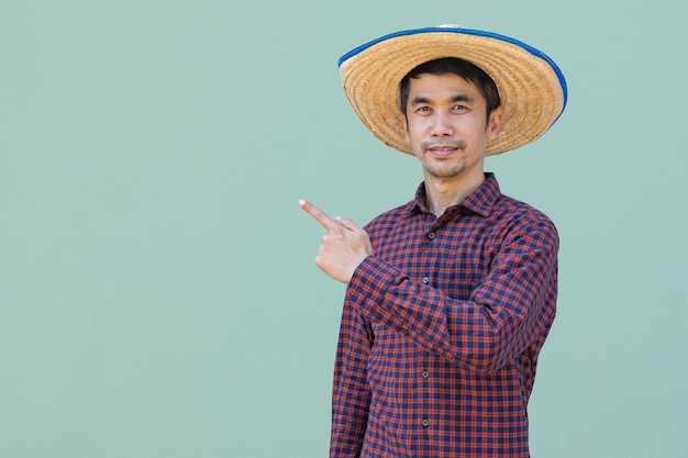 Azjatycki rolnik mężczyzna nosić czerwoną koszulę stojąc i wskazując widok z boku z zielonym tłem. Na białym tle obraz obcinania.
