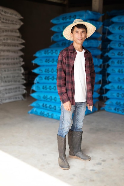 Azjatycki rolnik w czerwonej koszuli stoi z workiem nawozów chemicznych na magazynie