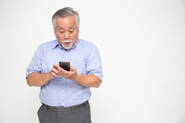 Azjatycki starszy mężczyzna używa smartphone i otrzymywający dobre wieści od wiadomości na mobilnym gadki zastosowaniu nad biel ścianą, no! No! I zdziwionym pojęciem