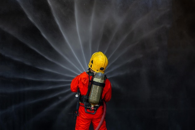 Azjatycki strażak na służbie gaszenia pożarów Azjatycki strażak rozpylający wodę pod wysokim ciśnieniem Strażak w ekwipunku przeciwpożarowym mundur spryskuje wodę z węża do gaszenia pożaru