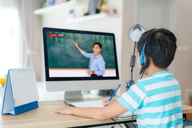 Azjatycki studencki chłopiec wideokonferencja e-learning z nauczycielem na komputerze w żywym pokoju w domu