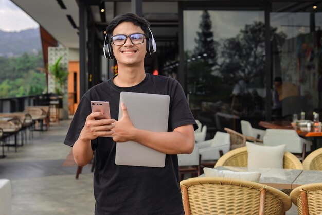 Azjatycki Student College'u Uśmiechający Się I Trzymający Telefon I Laptop W Kawiarni