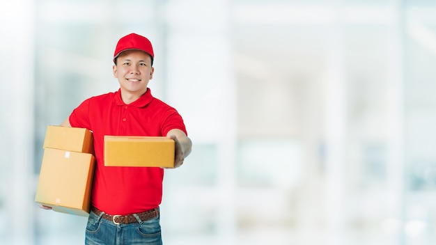 Azjatycki szczęśliwy dostawy mężczyzna ubrany w czerwoną koszulę przewożących paczki papierowe na białym tle