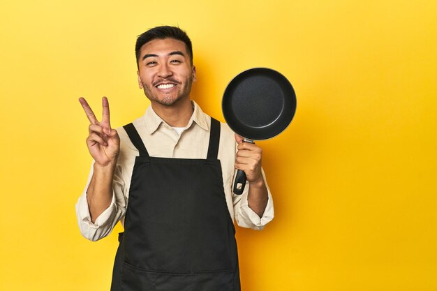 Azjatycki szef kuchni trzymający żółte tło studia pokazujące numer dwa z palcami
