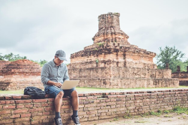 Zdjęcie azjatycki turysta pracujący i używający laptopa w historycznym parku sukhothai w tajlandii