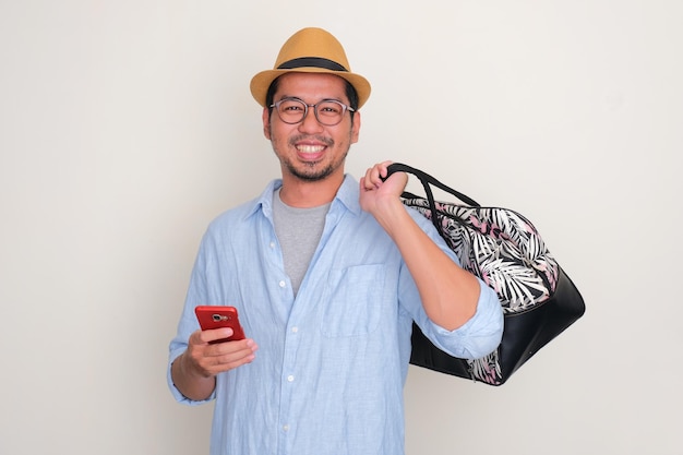 Azjatycki turysta przynosi podręczną torbę i trzyma telefon z radosnym wyrazem twarzy