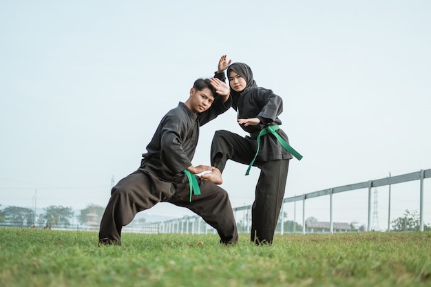 Azjatycki wojownik w mundurze pencak silat z niską pozą i zakapturzoną wojowniczką z jedną nogą uniesioną