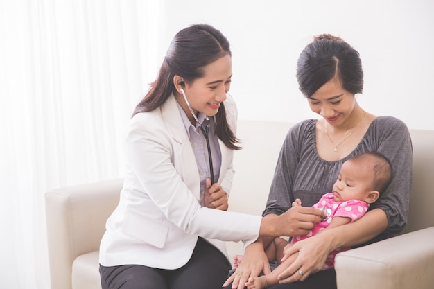 Azjatycki żeński pediatra egzamininuje dziewczynki na macierzystym podołku