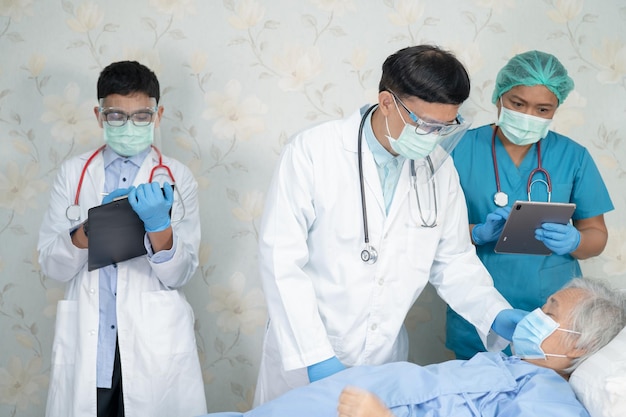 Azjatycki zespół lekarzy sprawdza starszą starszą pacjentkę pod kątem choroby, aby motywować nową normalną do leczenia infekcji Koronawirus Covid19 na oddziale szpitalnym