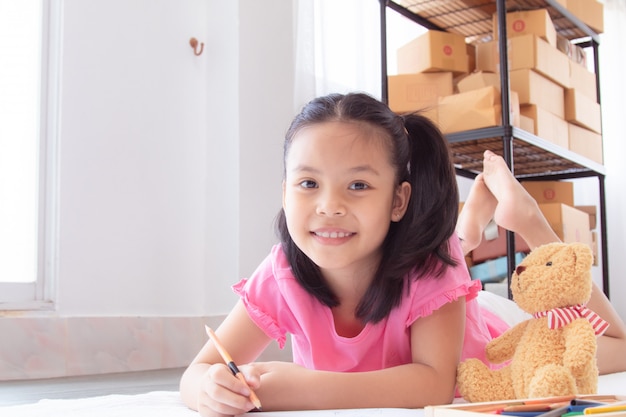 Azjatyckie domowe szkoły podstawowe urocze dzieci leżą na podłodze, odrabiając pracę domową za pomocą kredek, szczęśliwa wesoła dziewczyna spędza czas koncentrując się na rysowaniu okresu kwarantanny przed powrotem do szkoły