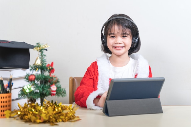 Azjatyckie dzieci dziewczynka sukienka Boże Narodzenie Santa Claus na czacie z przyjaciółmi na cyfrowym tablecie. Boże Narodzenie wakacje koncepcja Stock Photo