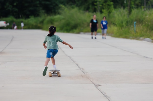 Azjatyckie dziecko dziewczyna uczy się na deskorolce na zewnątrz. Dziecko zabawy i gry na deskorolce na drodze w ciągu dnia. Aktywność dziecka i koncepcja sportów ekstremalnych.
