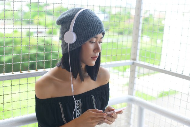 Azjatyckie dziewczyny słuchać muzyki ze słuchawek i jej smartphone.