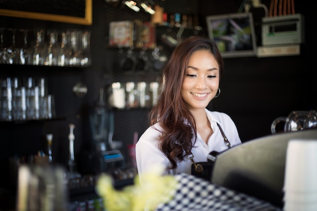 Azjatyckie kobiety Barista uśmiecha się i przy użyciu ekspres do kawy w kawiarni licznik - kobieta pracująca mały bu