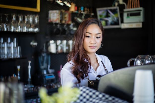 Azjatyckie kobiety Barista uśmiecha się kawową maszynę w sklep z kawą i używa - kontuar - kobieta pracująca małego biznesu właściciela jedzenia i napoju kawiarni pojęcie