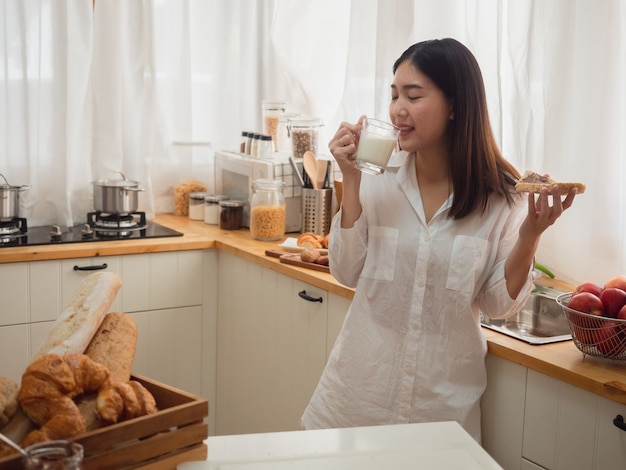 Azjatyckie kobiety jedzenie chleba i pić mleko w kuchni