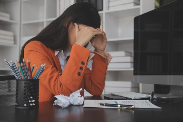 Azjatyckie kobiety siedzące w domowym biurze ze stresem i zmęczeniem oczu Zmęczona bizneswoman trzyma okulary i masuje mostek nosowy Są tablety laptopy i kawa