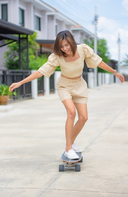 Zdjęcie azjatyckie kobiety stojącej na surfskate tło ulic i domów.