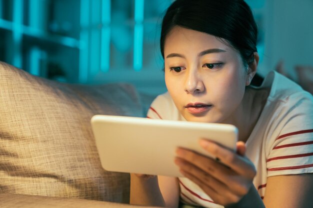 azjatyckie kobiety w nocy domu surfowanie po internecie z komputera typu tablet. inteligentna młoda dziewczyna ciężko pracująca e nauka języka online z nauczycielem za pomocą cyfrowego podkładki leżącej na kanapie przed snem o północy.