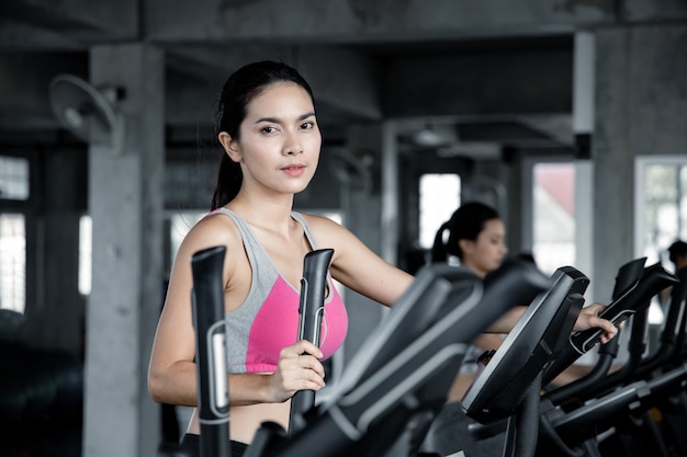 Azjatyckie młode kobiety z uśmiechem ćwiczą cardio na maszynie do ćwiczeń na siłowni.