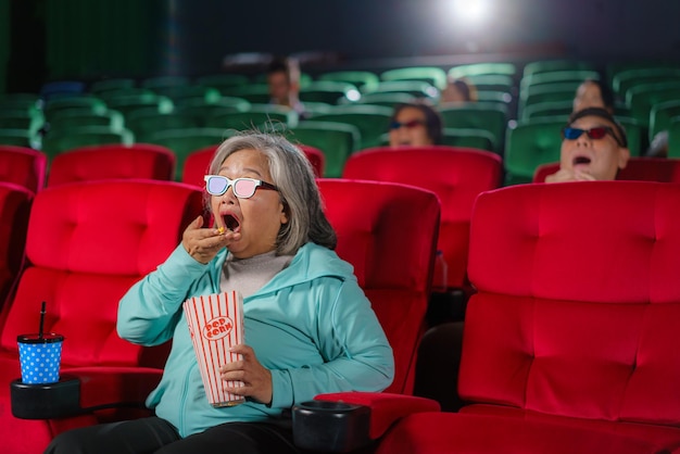 Azjatyckie starsze kobiety w okularach chętnie oglądają filmy 3D, delektując się popcornem w dłoni